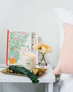 a white table topped with a vase filled with flowers next to a candle and book