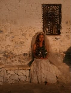 a woman in a wedding dress sitting on a stone bench