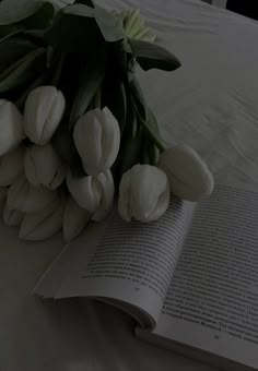 an open book sitting on top of a bed next to white tulips and leaves