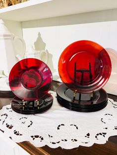 two red glass plates sitting on top of a white doily next to each other