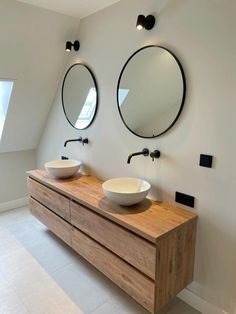 two round mirrors are on the wall above this double sink vanity in an attic bathroom