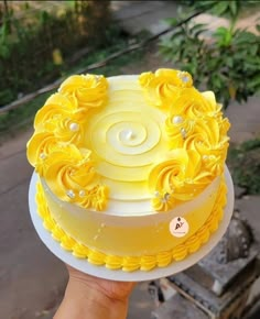 a hand holding a yellow and white cake