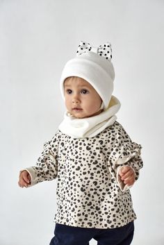 a baby wearing a white hat and scarf with black spots on it's face