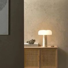 a white lamp sitting on top of a wooden cabinet next to a wall mounted painting