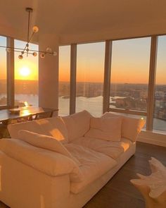 a living room filled with furniture and large windows overlooking the city at sunset or dawn