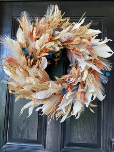 a wreath made out of dried feathers on a front door with blue and orange accents