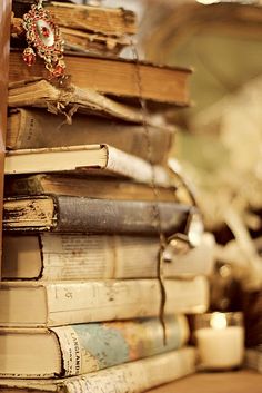 a stack of books sitting on top of a wooden table next to a white candle