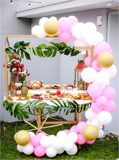 a table topped with lots of food and balloons in the shape of a circle on top of grass