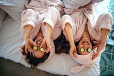 two women laying on top of a bed with cucumbers in their eyes and towels over their heads