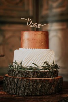 a three tiered wedding cake with greenery on top and the word taupo written in cursive font