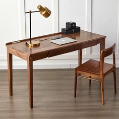 a wooden desk with a laptop on it and a chair next to it, in front of a white wall