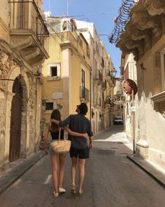 two people walking down an alley way with buildings in the background