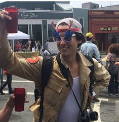 a man wearing glasses and holding up a red cup in the middle of a street