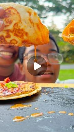 two people are eating pizza outside on the table and one person is holding up a piece of pizza