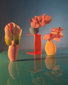 three vases with flowers in them sitting on a glass table next to each other