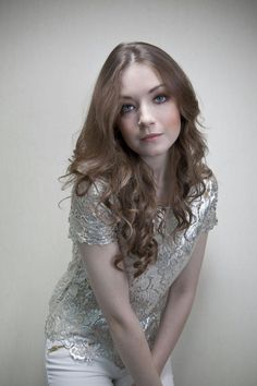 a woman with long hair posing for a photo in front of a white wall and holding her hands on her hips