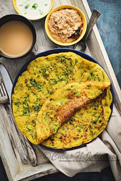 an omelet is on a plate next to two cups of coffee and spoons