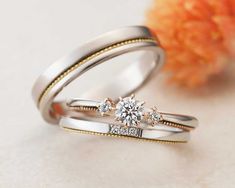 two wedding rings sitting next to each other on top of a white surface with flowers in the background