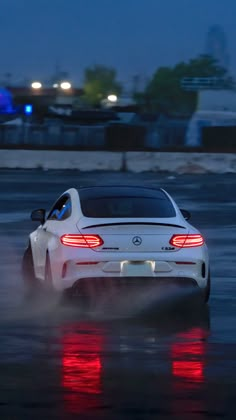 a white sports car driving down a wet road at night with red lights on it