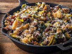 a skillet filled with cooked vegetables on top of a wooden table next to a spoon