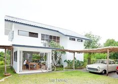 a car parked in front of a house with an awning on the roof and two people sitting at a table