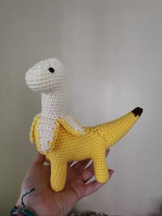 a hand holding a crocheted stuffed animal that looks like a dinosaur with a banana on its back