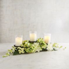 four candles with flowers and greenery on a table