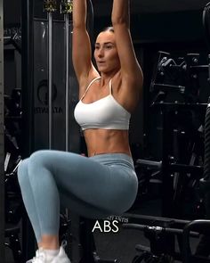 a woman is doing squats on a bar in the gym with her hands up