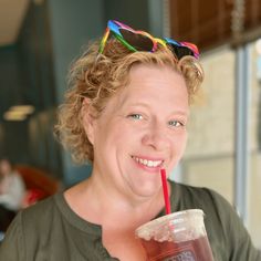 a woman with sunglasses on her head drinking from a plastic cup and smiling at the camera