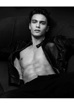 a man with no shirt sitting in a chair wearing a leather jacket and black pants