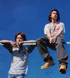 two young men sitting on top of a fence