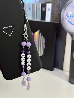 a pair of purple and white beaded earrings hanging from a cell phone holder on a table