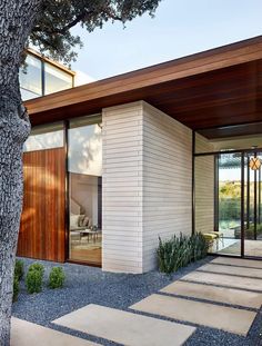 a modern house with wood and glass on the outside, along with stone steps leading up to the front door