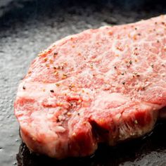 a piece of raw meat is cooking in a skillet on the stove with some seasoning