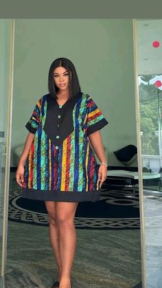 a woman standing in front of a mirror wearing a colorful shirt dress and black sandals