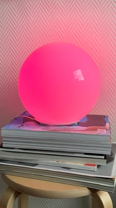 a pink ball sitting on top of stack of magazines in front of a pink wall