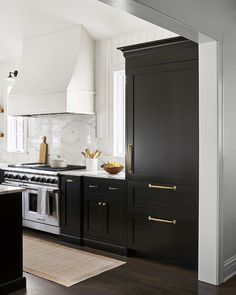 a kitchen with black cabinets and gold handles on the doors, white walls and wood flooring