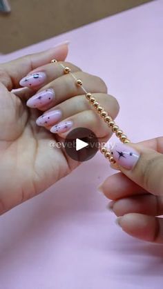 a woman holding onto a gold chain with pink and white designs on her nails,