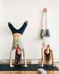 two women doing handstands on yoga mats in front of a white wall and wooden floor