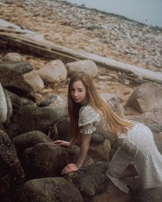 a woman is sitting on some rocks by the water with her hair blowing in the wind