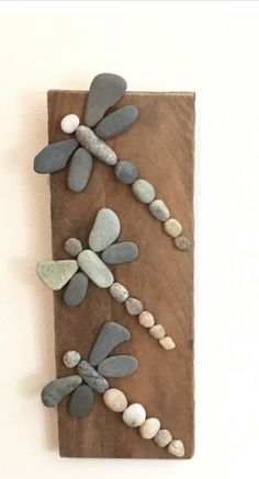 three dragonflys made out of stones on a wooden board