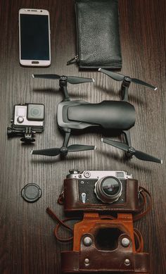 a camera, cell phone and other electronics are laid out on a wooden table next to each other