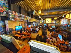 people are playing video games in a large room with wooden tables and couches on the floor