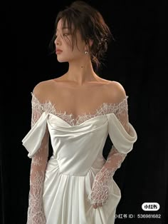 a woman in a white dress with long sleeves and lace on her arms, standing against a black background