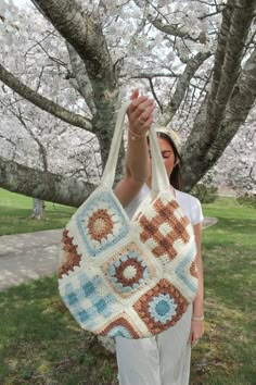 a woman holding up a crocheted bag in front of a tree