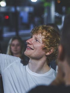 a young man is smiling and holding his cell phone up to the side while others look on