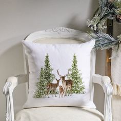 a white chair with a pillow on it and two deers in the woods behind it