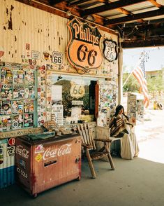 a woman sitting on a chair in front of a building with old signs and advertisements