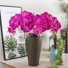 purple flowers in a brown vase on a table next to other plants and decor items