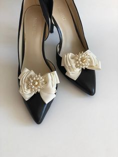 a pair of black and white high heel shoes with pearls on the bowknots